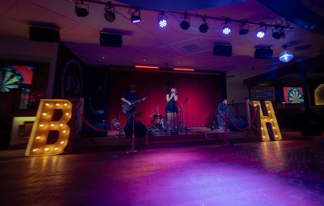 A wide view of a small venue stage under purple lights, with big light-up letters on the floor
