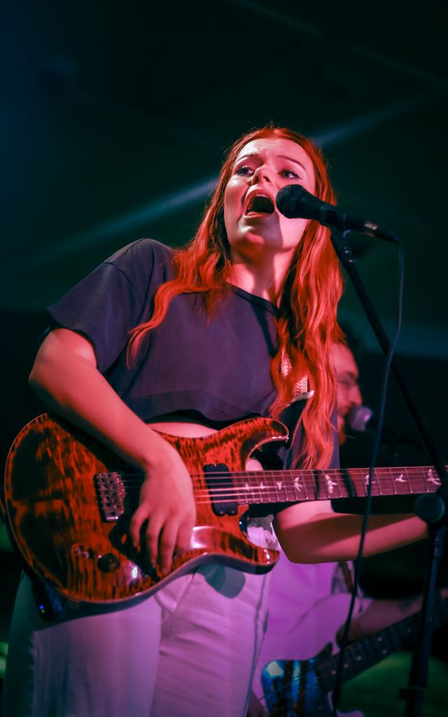 A guitarist with red hair singing under green and blue stage light
