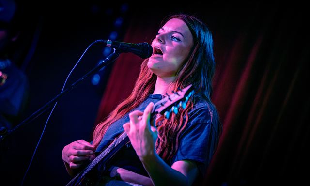 A singer and guitarist lit in pink and blue, mid-chorus