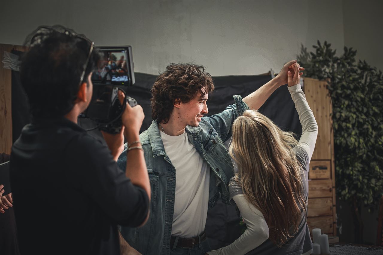 A camera operator filming two actors dancing