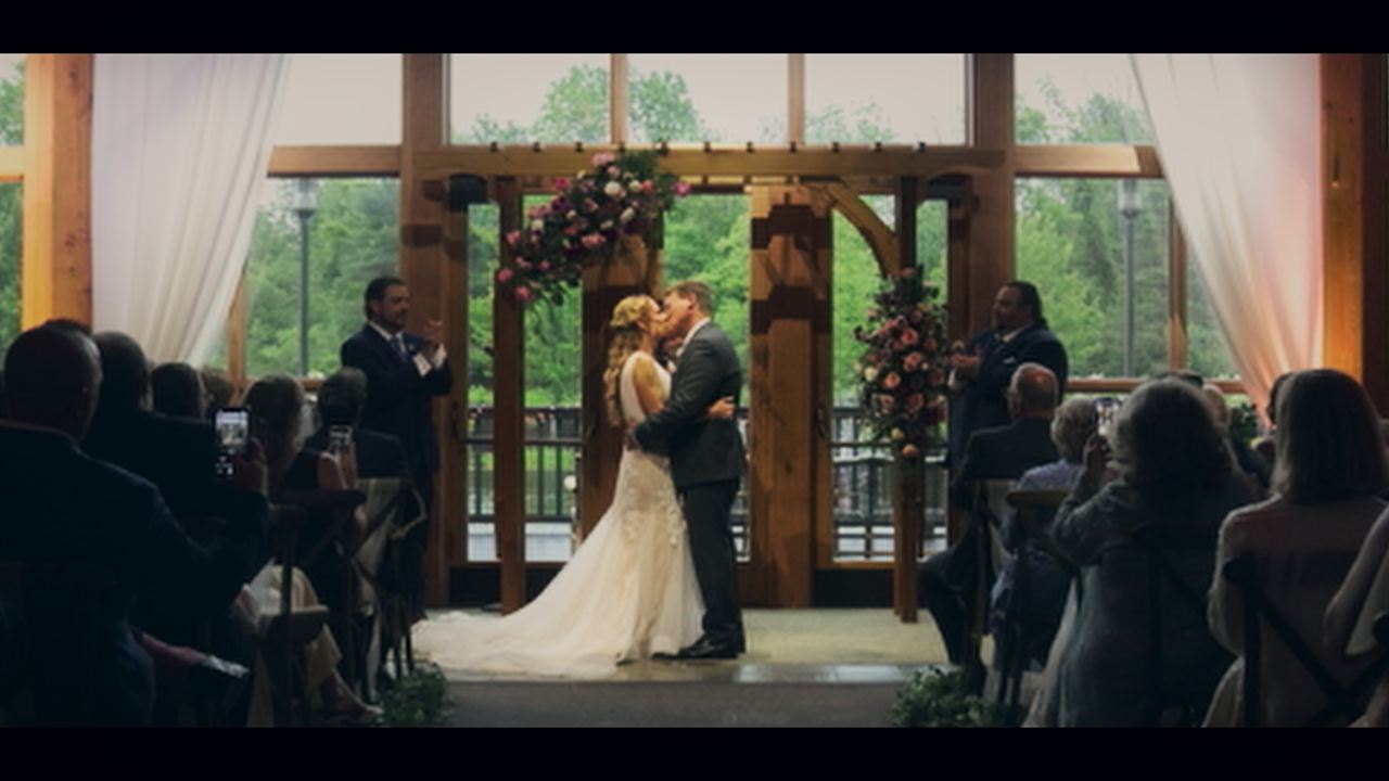 The couple kissing at the altar in a wooden hall while guests watch
