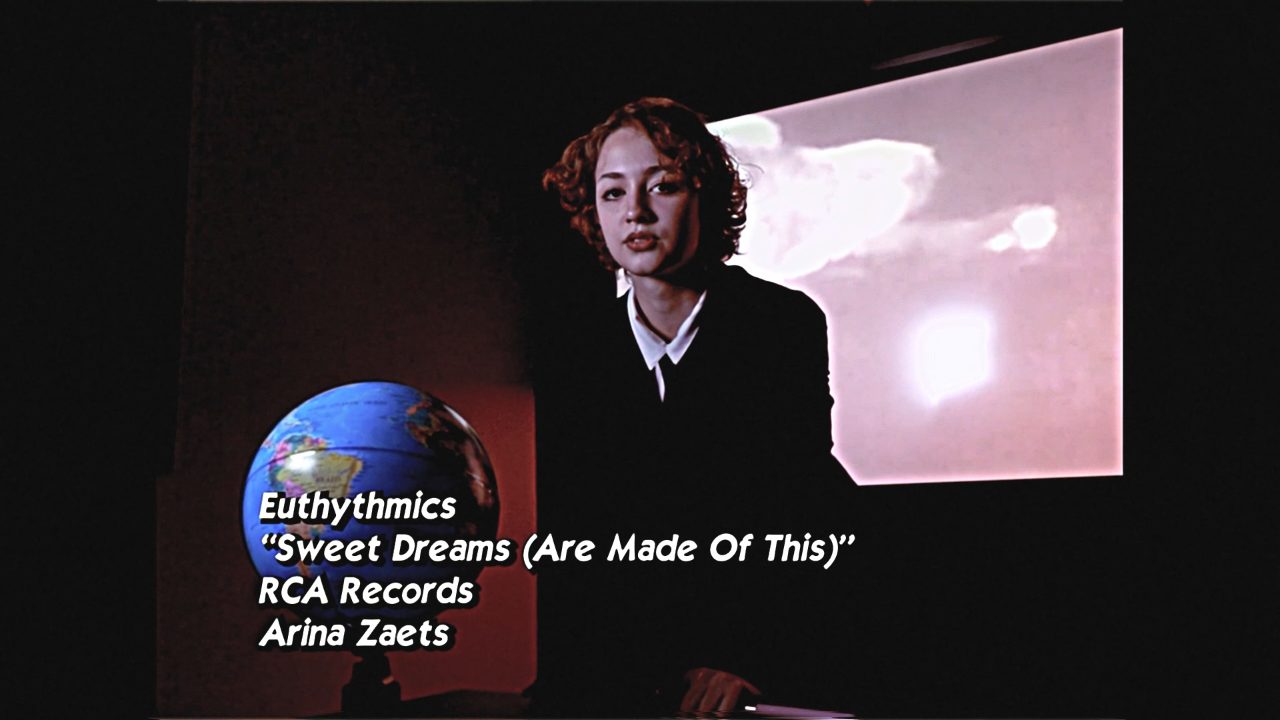 A singer in a dark suit standing in front of a projected screen